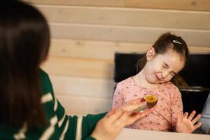 mère avec fille manger des fruits, elle donné une passion fruit. fille grimaça de le acide goût. photo