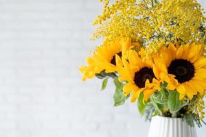 fleur de mimosa et tournesols dans blanc céramique vase sur blanc brique mur Contexte avec espace pour texte photo