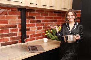 tutoriel de cuisine en ligne. photo recadrée main de femme fille utilisant un ordinateur portable pour vlog blogging tenant une casserole dans la cuisine moderne