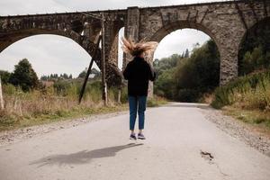 Jeune femme en marchant près vieux viaduc. touristique fille dans paysage campagne par le historique abandonné chemin de fer cambre pont viaduc dans vorokta, Ivano-frankivsk région, Ukraine photo