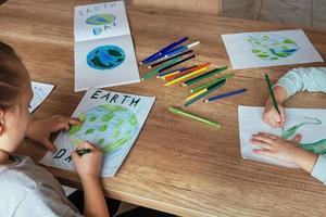 les enfants dessiner le planète Terre avec des crayons et feutre des stylos sur album feuilles pour Terre journée à leur Accueil tableau. le concept de protéger le environnement, paix sur Terre. photo