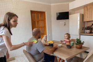 le famille pendant petit déjeuner dans le cuisine sur le premier de avril blagues et des bâtons papier poisson sur chaque autres dos. marrant famille blagues, traditions, avril imbécile journée fête photo