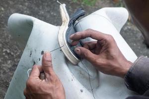 sélectif concentrer sur des sandales cette sont étant réparé par couture en utilisant fil et aiguilles, cette travail est appelé dans Indonésie une tukang sol sepatu, doux concentrer photo