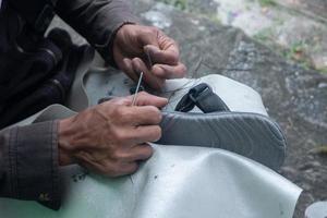 sélectif concentrer sur des sandales cette sont étant réparé par couture en utilisant fil et aiguilles, cette travail est appelé dans Indonésie une tukang sol sepatu, doux concentrer photo