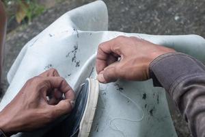 sélectif concentrer sur des sandales cette sont étant réparé par couture en utilisant fil et aiguilles, cette travail est appelé dans Indonésie une tukang sol sepatu, doux concentrer photo