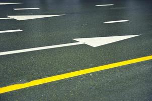 blanc flèches et Jaune lignes sur une humide asphalte route. photo