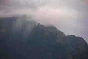 foncé atmosphérique surréaliste paysage avec une foncé rocheux Montagne de pointe dans faible des nuages dans une gris nuageux ciel. photo