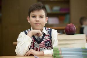 écolier à le bureau. garçon dans le salle de cours avec livres et un Pomme. secondaire école. retour à école. photo