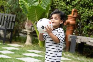 mignonne peu garçon en jouant football avec Balle en plein air sur football champ photo