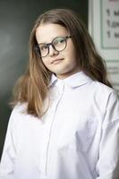 magnifique fille dans des lunettes de milieu école âge sur le Contexte de le tableau noir. photo