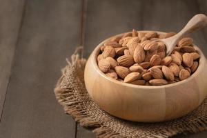 amandes écrou et bois cuillère dans bois tasse sur bois Contexte. photo