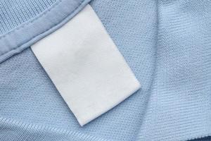 étiquette blanche de vêtements de soin de blanchisserie vierge sur fond de tissu de chemise bleue photo