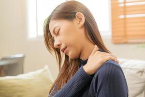 corps muscles rigide problème, asiatique Jeune attrayant femme, fille douleur avec retour douleur mal de travail, en portant masser frottement épaule blesser ou douloureux, douloureux séance sur canapé à maison. soins de santé personnes. photo