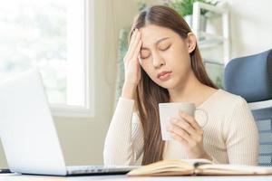 souffrir, attrayant asiatique Jeune femme, fille en portant tasse, tasse de café, ayant mal de tête, migraine après en buvant fort caféine ou thé tandis que travail de maison, visage expression stress, maladies gens photo