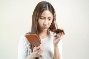 sérieux, inquiet asiatique Jeune femme, fille en portant brosse, spectacle sa peigne, brosse à cheveux avec longue perte cheveux problème après brossage, cheveux tomber en dehors sur sa main dans vivant chambre. santé se soucier, beauté traitement. photo