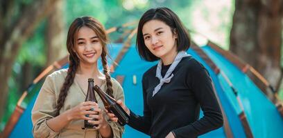 les jeunes femmes applaudissent et boivent une boisson devant la tente de camping photo