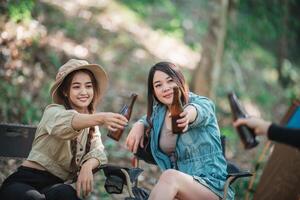 les jeunes femmes applaudissent et boivent une boisson devant la tente de camping photo