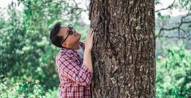 portrait d'un homme asiatique heureux étreignant un arbre dans la forêt photo