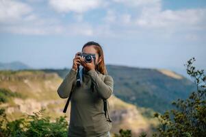 Jeune trekking femelle utilisation caméra la photographie sur rocheux Montagne de pointe photo