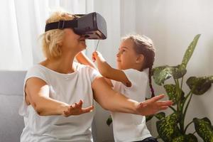 grand-mère et petite fille. content vieux femme en jouant virtuel réalité avec peu fille à maison. vr, augmenté réalité vidéo et technologie. photo