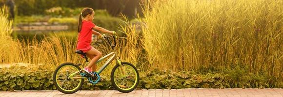 enfant équitation vélo. enfant vélo dans ensoleillé parc. peu fille profiter bicyclette balade sur sa façon à école chaud été journée. enfant d'âge préscolaire apprentissage à équilibre vélo sport pour enfants. photo