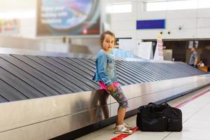 le fille séance à le aéroport sur le ruban pour bagage, lequel est situé près le réception. Regardez une façon