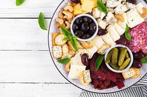 antipasto plat avec basturma, salami, bleu fromage, des noisettes, cornichons et Olives sur une blanc en bois Contexte. Haut voir, aérien photo
