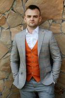 portrait de le jeune marié dans une gris costume et un Orange gilet photo