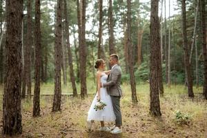 Jeune couple la mariée dans une blanc court robe et jeune marié dans une gris costume dans une pin forêt photo