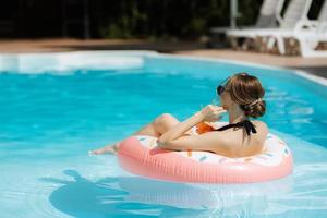 une fille dans une noir maillot de bain flotteurs dans une bleu bassin photo