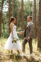 Jeune couple la mariée dans une blanc court robe et jeune marié dans une gris costume dans une pin forêt photo