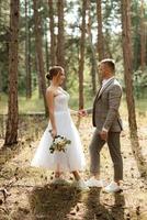 Jeune couple la mariée dans une blanc court robe et jeune marié dans une gris costume dans une pin forêt photo