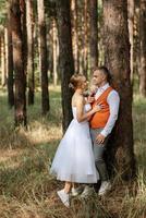 Jeune couple la mariée dans une blanc court robe et jeune marié dans une gris costume dans une pin forêt photo