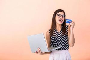 portrait de souriant content femme dans décontractée vêtements en portant crédit carte et portable avec des lunettes isolé plus de pêche Contexte. en ligne achats concept photo