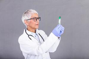 femelle médecin ou technicien en portant tester tube médical équipement. du sang ou virus test. Sénior médecin femme travail avec du sang échantillons dans tester tuyaux, fermer photo