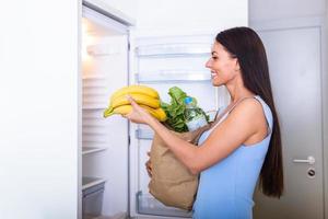 en bonne santé en mangeant concept. régime. magnifique Jeune femme près le frigo avec en bonne santé aliments. des fruits et des légumes dans le réfrigérateur. végétalien nourriture