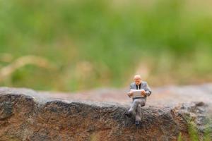 homme d'affaires miniature, lisant un journal sur un rocher avec un fond de nature photo