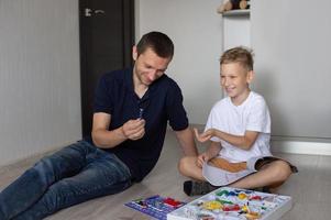 une mignonne garçon dans une blanc T-shirt recueille un électrique designer avec le sien papa dans le pièce photo