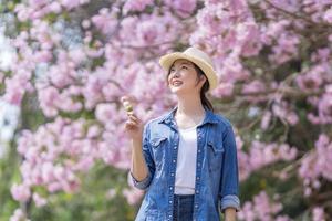 asiatique femme en portant le sucré hanami dango dessert tandis que en marchant dans le parc à Cerise fleur arbre pendant printemps Sakura Festival avec copie espace photo