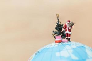 Père Noël miniature tenant des cadeaux pour les enfants sur un globe, joyeux Noël concept photo