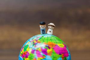 Poupées en bois miniatures sur un globe avec un fond en bois photo
