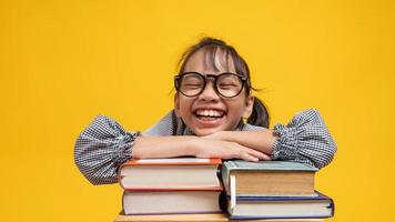 étudiante thaïlandaise avec des lunettes s'appuyant sur une pile de livres en souriant et en regardant la caméra avec un fond jaune photo