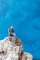 homme d & # 39; affaires miniature assis sur un rocher avec un fond bleu photo