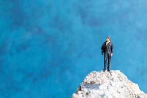 homme d & # 39; affaires miniature debout sur un rocher avec un fond bleu photo