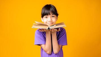jeune fille asiatique, sourire, dans, chemise violette, tenue, livre ouvert, dans, studio, à, fond jaune photo
