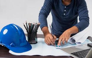 architecte travaillant sur un plan à côté d'un ordinateur portable, d'un casque, d'une tasse de crayons et de papier roulé