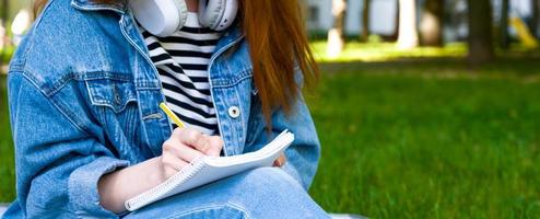 une fille méconnaissable prend des notes dans un cahier dans le parc. apprentissage à distance. université, collège, éducation scolaire photo