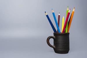 coloré marrant des crayons dans une argile tasse sur une gris arrière-plan, coloré des crayons dans une argile verre. photo