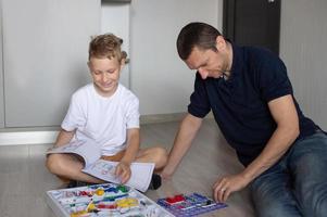 une mignonne garçon dans une blanc T-shirt recueille un électrique designer avec le sien papa dans le pièce photo