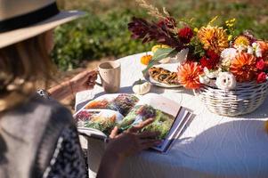 une femme flips par une livre et les boissons une chaud boisson à une table avec fleurs sur le rue photo